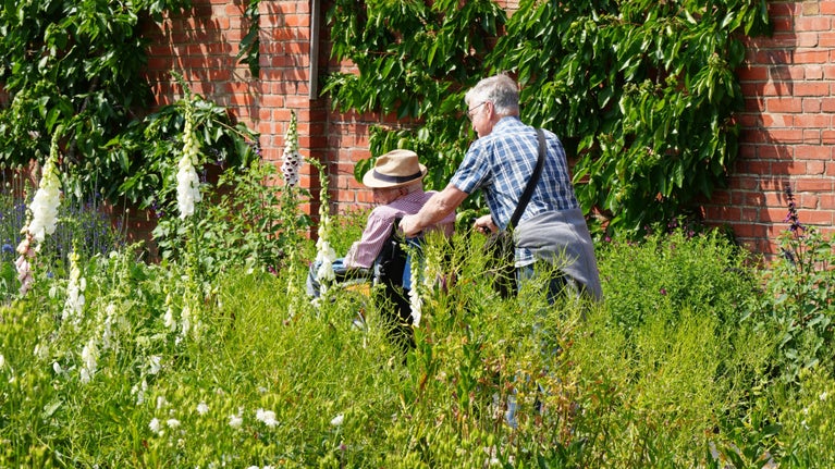 Visitor in a wheelchair is pushed by a carer in the Walled Garden at Chartwell, Kent
